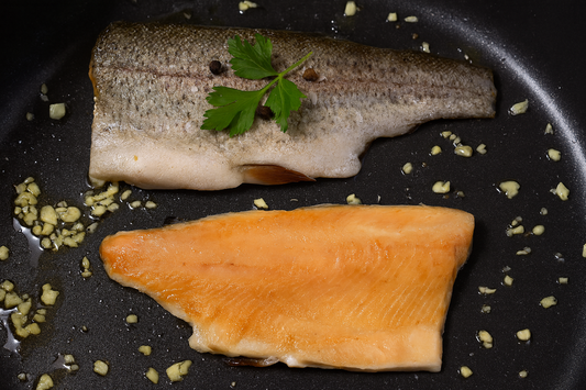 Two pieces of fish on a black pan with garlic and parsley.
