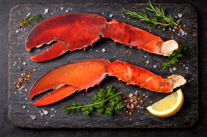 Two lobster claws on a dark wooden board with herbs and lemon